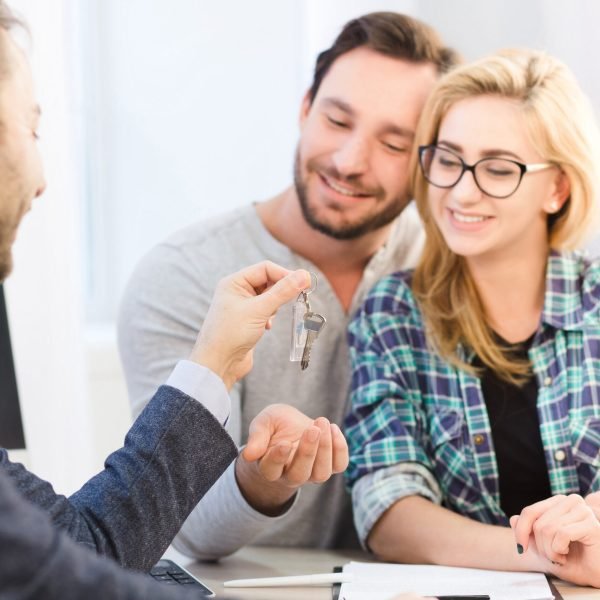 Dealership concept. Bank concept. Toned of sales manager ready to give key to young couple in love after signing agreement or contract for purchase or sale.
